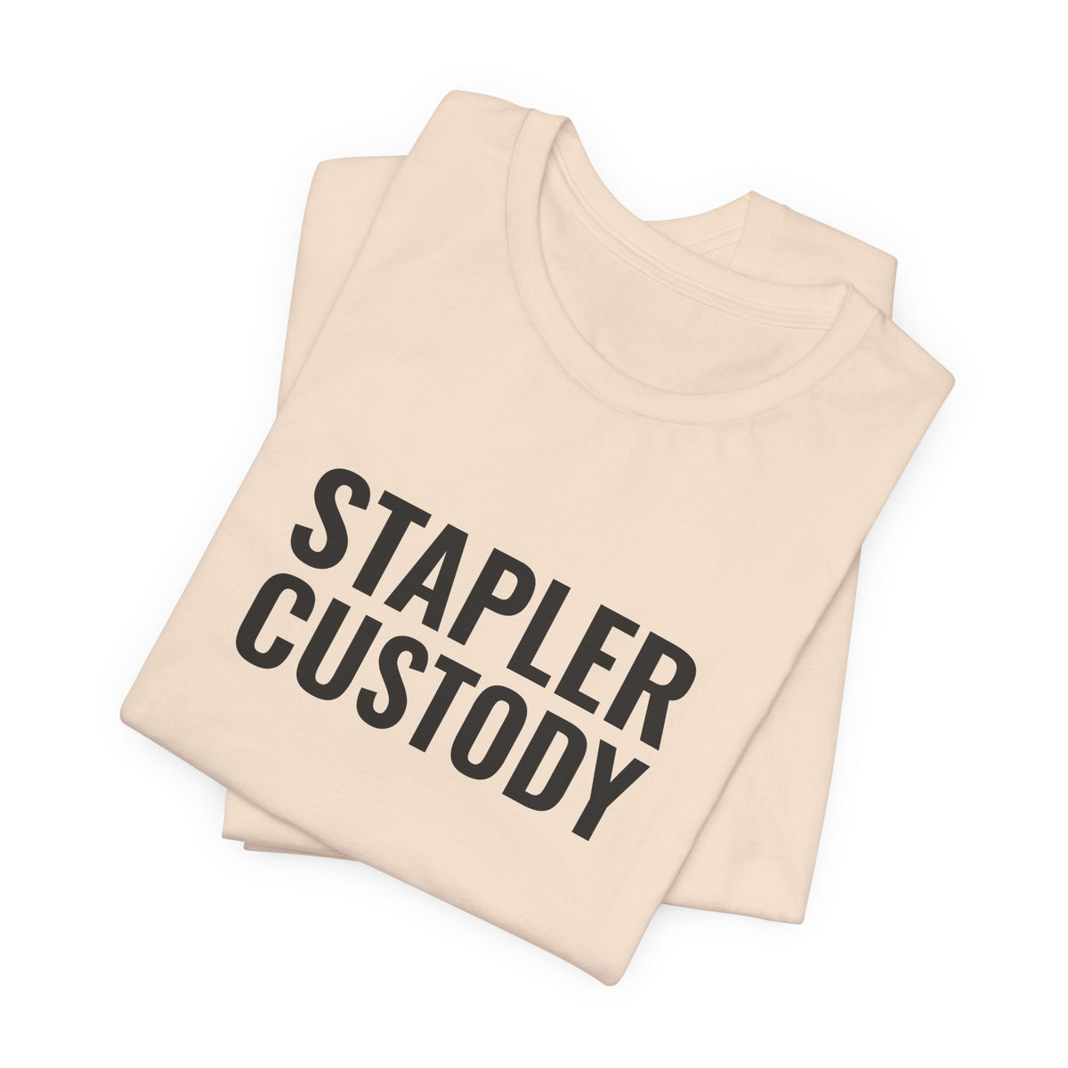 Folded soft cream tee showing the “Stapler Custody” print