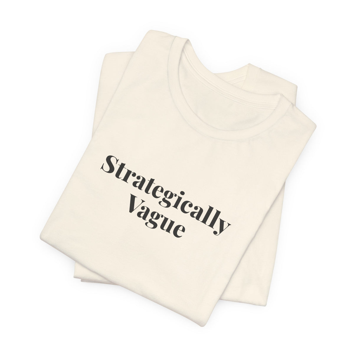 Folded natural tee showing the “Strategically Vague” print