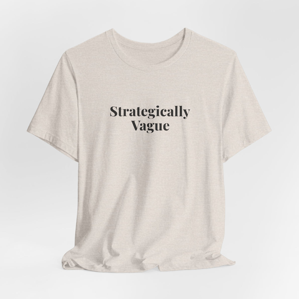 The heather dust “Strategically Vague” tee hanging on a hanger